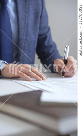 Closeup of businessman signing a contract with elegant pen, wearing a blue suit and a wristwatch, sitting at a white desk in office. Business people concept 132706058
