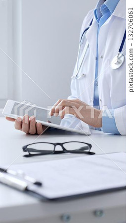 Unknown doctor woman wearing lab coat and stethoscope using digital tablet with laptop and medical records on desk in medical office, showcasing modern healthcare technology. Medicine concept Unknown doctor woman wearing lab coat and stethoscope using digital tablet with laptop and medical records on desk in medical office, showcasing modern healthcare technology. Medicine concept 132706061