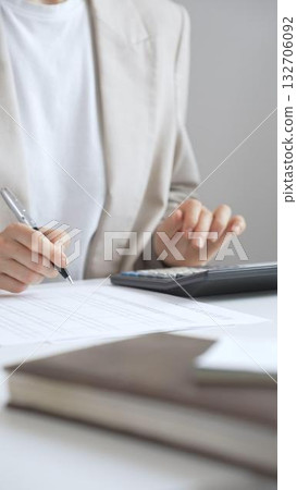 Businesswoman is calculating annual tax using calculator and taking notes in the office, managing domestic budget and checking financial documents. Audit and taxes in business 132706092