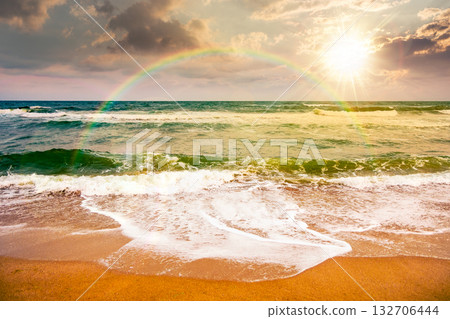 black sea waves crashing sandy beach at sunset. summer vacation on a windy weather under cloudy sky in evening light. view of dramatic seascape. storytelling image under the rainbow 132706444