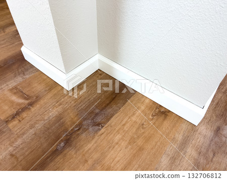 Detailed view of white corner trim installed on natural wood-style vinyl plank flooring. Perfect for construction websites, flooring product advertising, and DIY renovation guides. 132706812