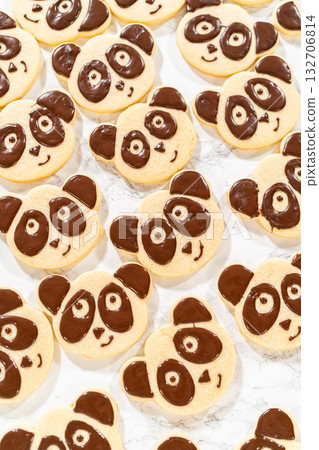 Overhead view of a batch of panda cookies with completed chocolate icing designs for the Chocolate Royal Icing Recipe. Each cookie features a cute panda face, giving a uniform and adorable look. 132706814