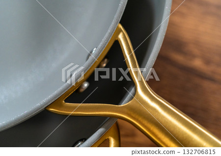 Extreme close-up showing the joint between the gold handle and the ceramic frying pan. The image highlights metallic finish, rivets, and craftsmanship. 132706815