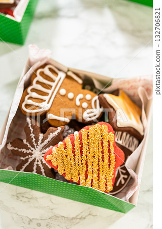 Captured from a close-up perspective, green holiday gift boxes filled with decorated Christmas cookies are neatly arranged with parchment lining. The festive assortment includes mitten, tree, and star Captured from a close-up perspective, green holiday gift boxes filled with decorated Christmas cookies are neatly arranged with parchment lining. The festive assortment includes mitten, tree, and star 132706821