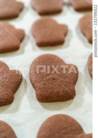Front-facing view of freshly baked Pale Gingerbread Cookies in mitten shapes resting on a parchment-lined tray, just out of the oven. 132706822