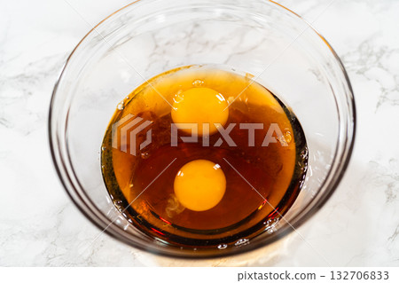 Two large eggs cracked into a glass bowl, combined with molasses. This mixture adds richness, moisture, and depth of flavor to the Classic Red Gingerbread Dough. 132706833