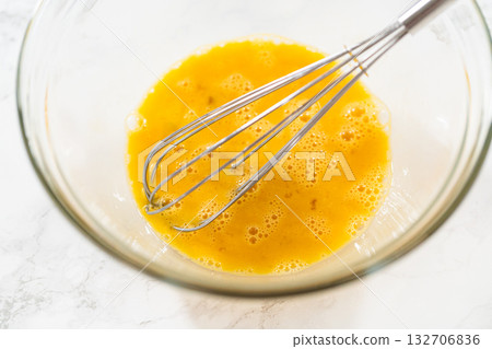 Close-up view of a whisk resting in a bowl of beaten eggs, prepared for Classic Sugar Cookie Dough. The eggs are well-mixed and slightly frothy, ready to be incorporated into the dough mixture as part 132706836