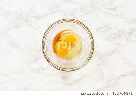 Glass bowl with beaten eggs and vanilla extract for Classic Sugar Cookie Dough on a marble surface, with a whisk resting in the mixture. This step showcases the wet ingredient preparation essential 132706871