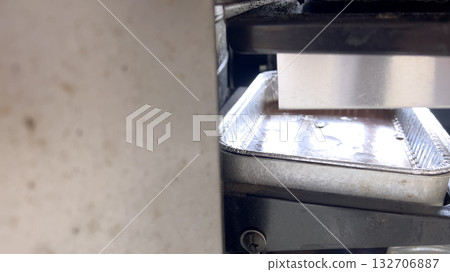 Close-up of a hand sliding a disposable aluminum grease tray into the designated slot beneath the grill. The tray is partially filled with used cooking residue. Close-up of a hand sliding a disposable aluminum grease tray into the designated slot beneath the grill. The tray is partially filled with used cooking residue. 132706887