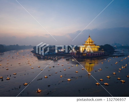 A stunning view of an illuminated riverside temple surrounded by hundreds of floating diyas at dusk. The calm water reflects the golden lights, creating a serene and spiritual atmosphere. A stunning view of an illuminated riverside temple surrounded by hundreds of floating diyas at dusk. The calm water reflects the golden lights, creating a serene and spiritual atmosphere. 132706937