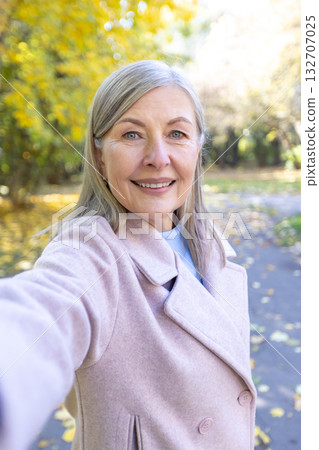 Senior woman with gray hair smiling and taking a selfie on a sunny autumn walk in a colorful park, enjoying a cheerful, relaxed moment among vivid fall leaves with her smartphone Senior woman with gray hair smiling and taking a selfie on a sunny autumn walk in a colorful park, enjoying a cheerful, relaxed moment among vivid fall leaves with her smartphone 132707025