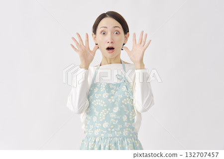 一位穿著圍裙、站在白色背景前的女士，顯得驚訝。 132707457