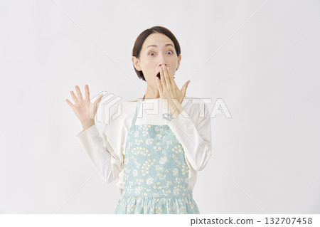 一位穿著圍裙、站在白色背景前的女士，顯得驚訝。 132707458