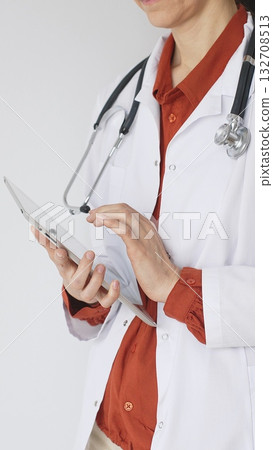 Unknown professional woman doctor, wearing white coat over a brick-red blouse and a stethoscope, is using a digital tablet, suggesting innovative healthcare practices in medicine. Health care concept 132708513