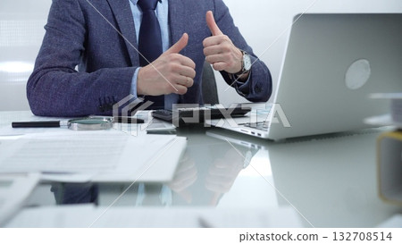 Businessman wearing blue suit is working with laptop while sitting and gesturing with his hands at the glass table in office background. Low lighting, close-up view. Business people and audit concept Businessman wearing blue suit is working with laptop while sitting and gesturing with his hands at the glass table in office background. Low lighting, close-up view. Business people and audit concept 132708514