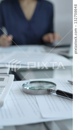 Businesswoman wearing blue dress is working with laptop, calculator and documents in a professional office setting. Low lighting, close-up vertical view. Business people, audit concept 132708648