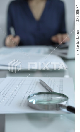 Businesswoman wearing blue dress is working with laptop, calculator and documents in a professional office setting. Low lighting, close-up vertical view. Business people, audit concept Businesswoman wearing blue dress is working with laptop, calculator and documents in a professional office setting. Low lighting, close-up vertical view. Business people, audit concept 132708674