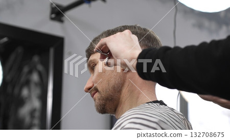 Professional barber trimming blond heard male client's hair with scissors and comb, creating precise modern hairstyle inside contemporary grooming salon Professional barber trimming blond heard male client's hair with scissors and comb, creating precise modern hairstyle inside contemporary grooming salon 132708675