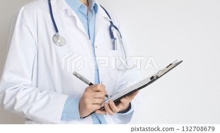 Close up of doctor woman wearing stethoscope and white coat over blue blouse is standing and writing on a black clipboard, representing medical expertise and patient care. Medicine concept Close up of doctor woman wearing stethoscope and white coat over blue blouse is standing and writing on a black clipboard, representing medical expertise and patient care. Medicine concept 132708679