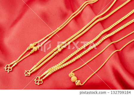Gold chain necklace on red silk textile. 132709184