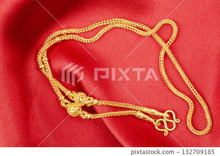 Gold chain necklace on red silk textile. 132709185