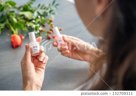 A woman compares two gel nail polish bottles labeled TPO and TPO free. The concept highlights awareness of harmful ingredients like Trimethylbenzoyl Diphenylphosphine Oxide. 132709311