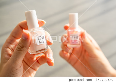 A woman compares two gel nail polish bottles labeled TPO and TPO free. The concept highlights awareness of harmful ingredients like Trimethylbenzoyl Diphenylphosphine Oxide. A woman compares two gel nail polish bottles labeled TPO and TPO free. The concept highlights awareness of harmful ingredients like Trimethylbenzoyl Diphenylphosphine Oxide. 132709329