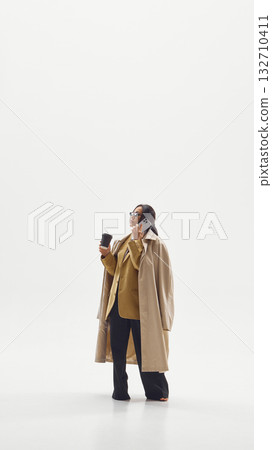 Modern businesswoman in beige coat multitasking with phone and coffee representing leadership and focus Modern businesswoman in beige coat multitasking with phone and coffee representing leadership and focus 132710411