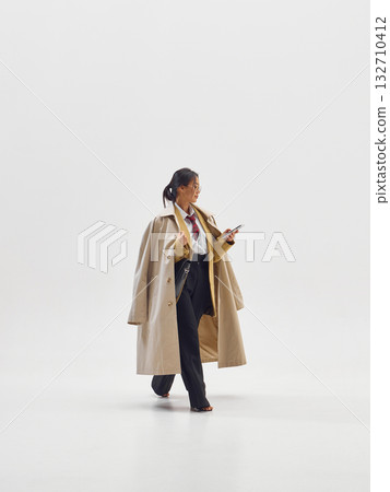 Confident woman in trench coat using smartphone symbolizing leadership and balance in modern business 132710412