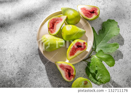 Sweet green figs in a plate a on a gray concrete background with leaves and sunlight. 132711176