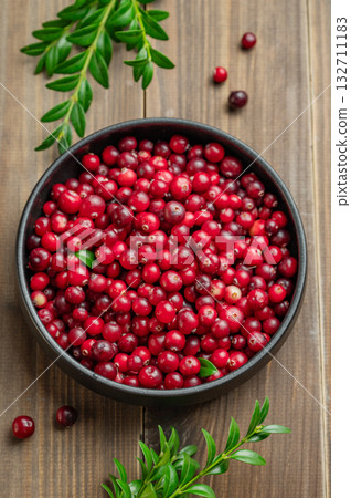 layout of fresh cranberries in a dark bowl on a wooden background with green branch. layout of fresh cranberries in a dark bowl on a wooden background with green branch. 132711183