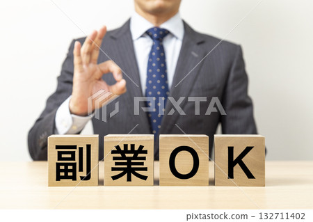 一名商人擺出「OK」的手勢,旁邊立著一塊寫著「副業OK」的牌子。 一名商人擺出「OK」的手勢,旁邊立著一塊寫著「副業OK」的牌子。 132711402