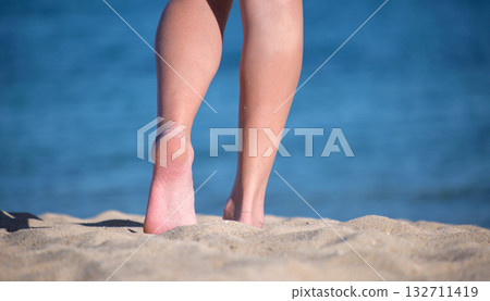 Close up of female feet walking barefoot on white grainy sand of golden beach on blue ocean water background Close up of female feet walking barefoot on white grainy sand of golden beach on blue ocean water background 132711419