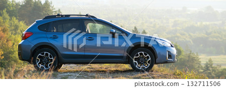 Blue off road car at dawn on grassy hill on distant foggy city landscape background. Extreme travel on a SUV automobile Blue off road car at dawn on grassy hill on distant foggy city landscape background. Extreme travel on a SUV automobile 132711506