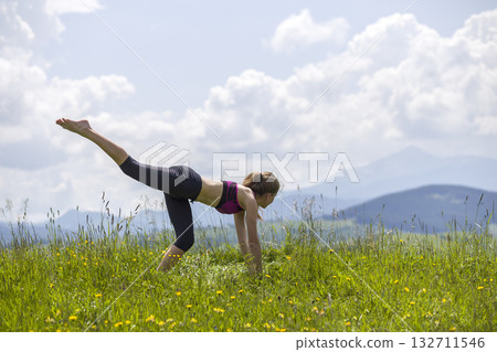 Attractive slim young woman doing yoga exercises outdoors on copy space background of mountains. Attractive slim young woman doing yoga exercises outdoors on copy space background of mountains. 132711546