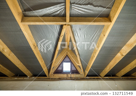 Attic of a building with wooden beams of a roof structure and a small window. Attic of a building with wooden beams of a roof structure and a small window. 132711549