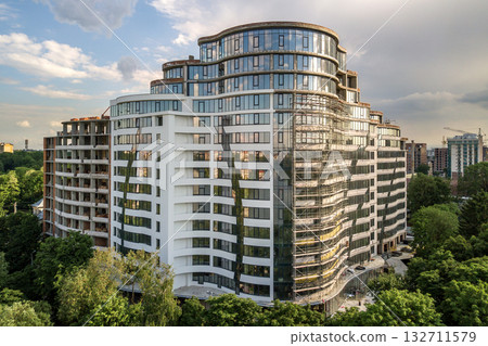 Apartment or office tall building under construction. Brick walls, glass windows, scaffolding and concrete support pillars Apartment or office tall building under construction. Brick walls, glass windows, scaffolding and concrete support pillars 132711579