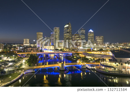 American city skyline with brightly illuminated high commercial buildings and bridge over Hillsborough river. Night urban landscape of downtown district of Tampa in Florida, USA. 132711584