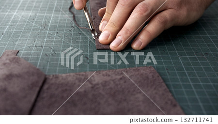 Craftsman using edge tool on leather strip for handmade leather goods production 132711741