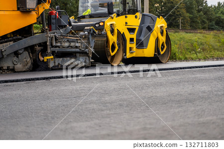 Close-up of yellow asphalt paving machine working on fresh road surface 132711803