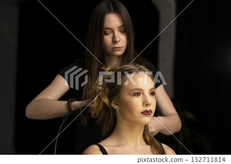 Hairstylist curling hair with hot iron for young woman in professional salon 132711814