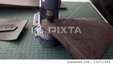 Leather craftsman using press machine for punching holes in brown leather piece Leather craftsman using press machine for punching holes in brown leather piece 132711841