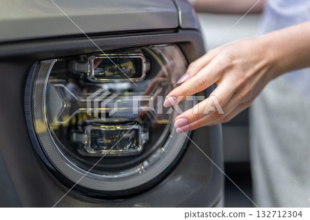 A close-up shot of a woman's hand touching a modern car headlight A close-up shot of a woman's hand touching a modern car headlight 132712304