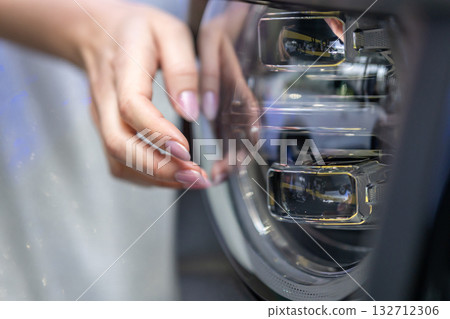 A close-up shot of a woman's hand touching a modern car headlight 132712306