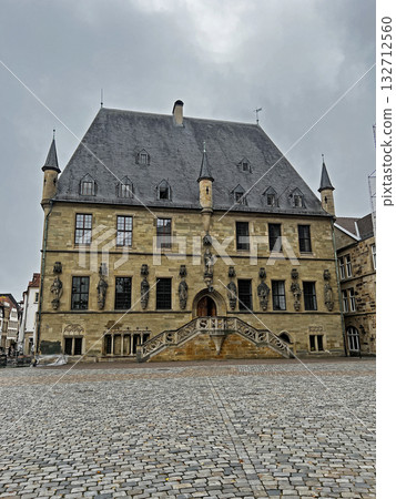 Osnabruk historic Town Hall features a slate roof, towers, stone statues, and central stairs leading to the entrance, set on a cobbled square. Osnabruk historic Town Hall features a slate roof, towers, stone statues, and central stairs leading to the entrance, set on a cobbled square. 132712560