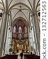 The spacious interior of Osnabruk cathedral reveals soaring gothic arches, tall windows with stained glass, a crucifix, and an ornately gilded altar. 132712563
