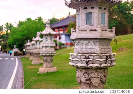 Stone lanterns line a path in Nanshan Park, surrounded by greenery. Chinese architecture is visible in the background. Stone lanterns line a path in Nanshan Park, surrounded by greenery. Chinese architecture is visible in the background. 132714068