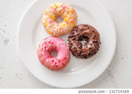 Pink white and chocolate glazed donuts arranged neatly on clean minimalist white plate Pink white and chocolate glazed donuts arranged neatly on clean minimalist white plate 132714169