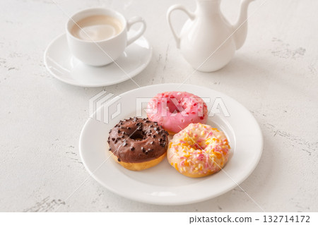 Trio of glazed donuts with coffee cup and pitcher in bright morning light Trio of glazed donuts with coffee cup and pitcher in bright morning light 132714172