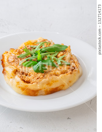 Circular lasagna presentation topped with fresh arugula served on elegant white plate 132714173